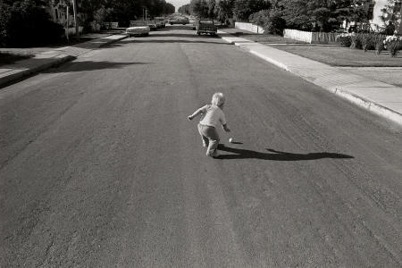 1977 Perfect Timing - Car at the end of the road is perfectly centered as the boy retrieves the ball.